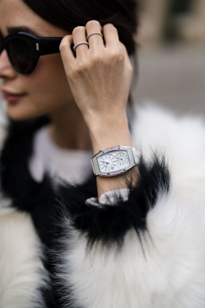 Снимката представя жена с елегантно кожено палто и бял дамски часовник с камъни