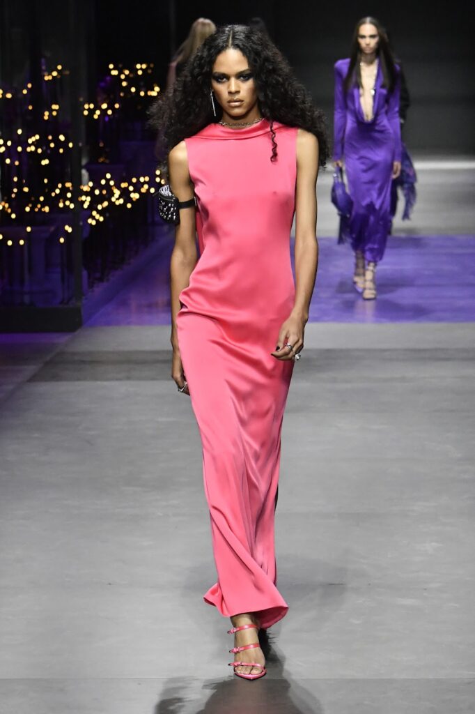 Моделът е облечен с дълга сатенена розова рокля без ръкави